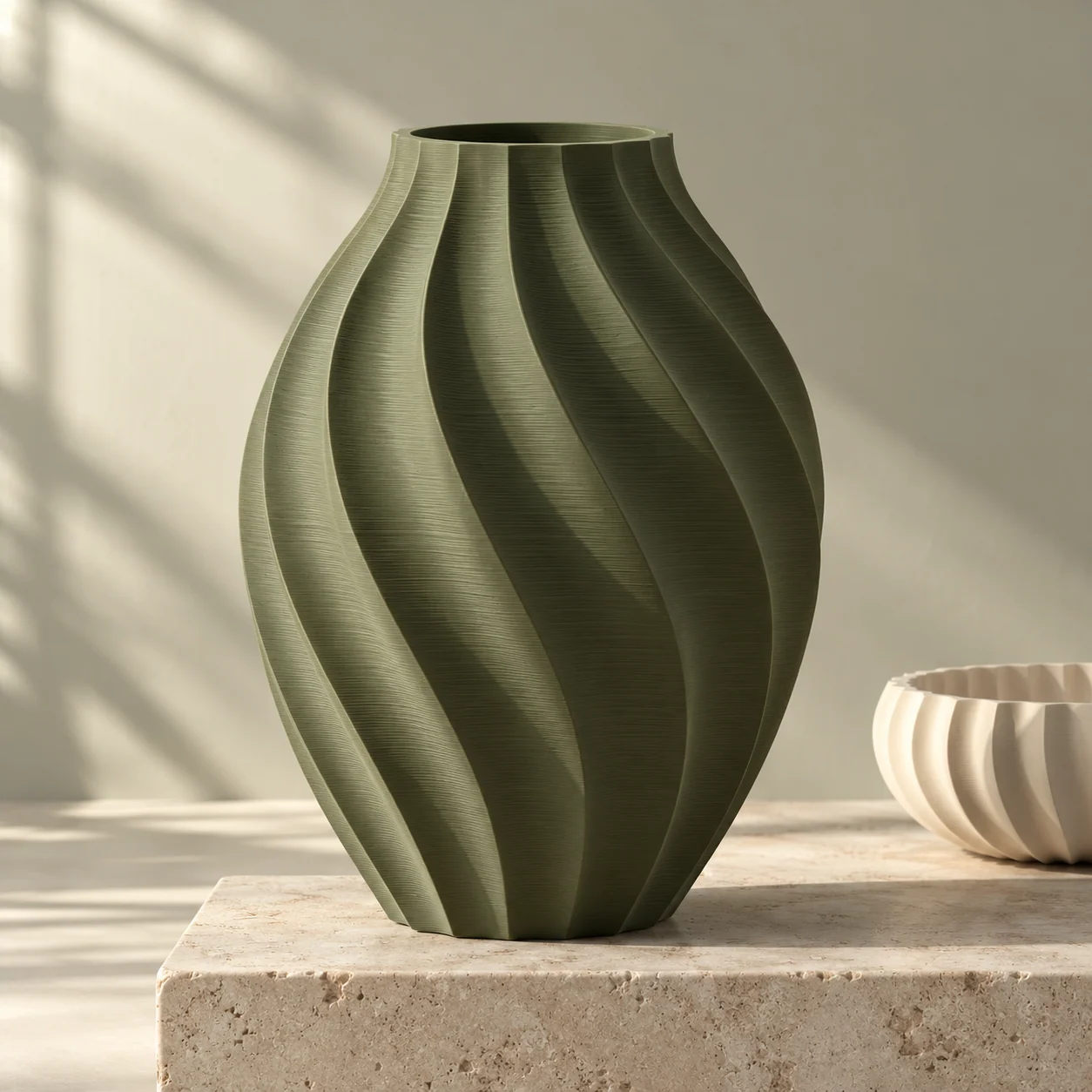 Sculptural olive green Ripple Vase beside an ivory bowl on a stone plinth